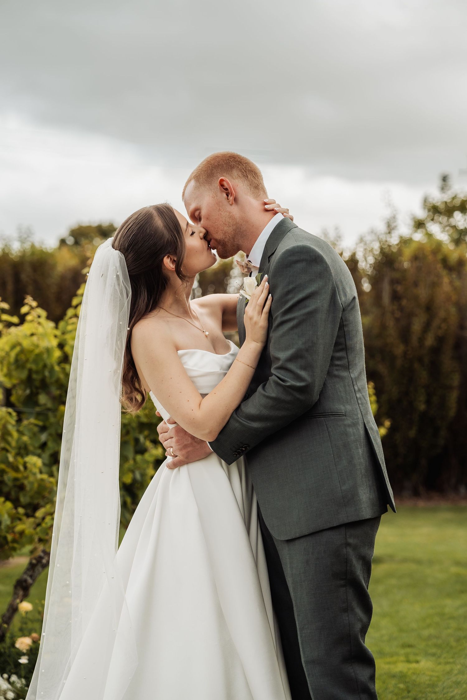 Bride and groom share a romantic kiss while embracing in a lush garden setting on their wedding day.