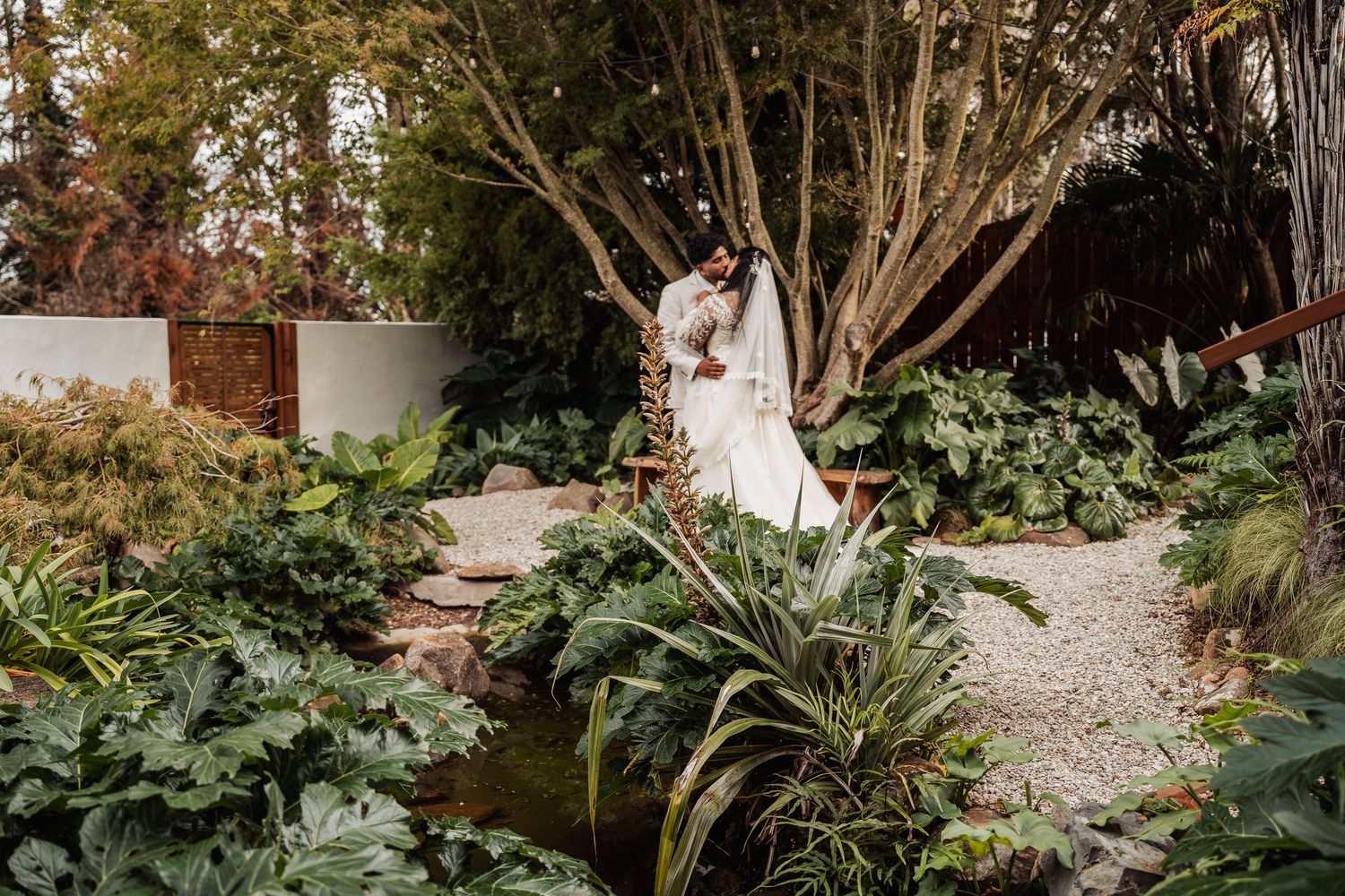Bride and groom embracing in lush garden setting surrounded by tropical greenery on wedding day.