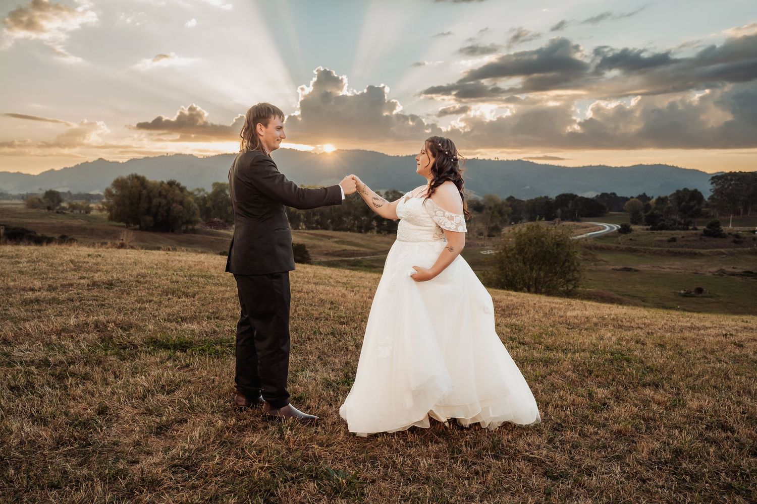 Bride and groom dancing in a golden field at sunset with mountain views behind them.