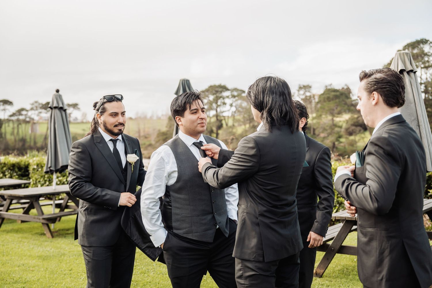 A group celebrates in black attire at an outdoor gathering with picnic tables in the background.