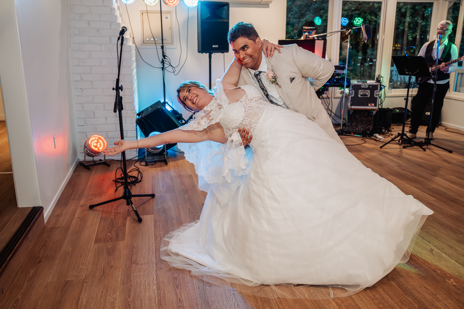 Playful wedding dance scene with dramatic dip move on hardwood floor at indoor reception venue.