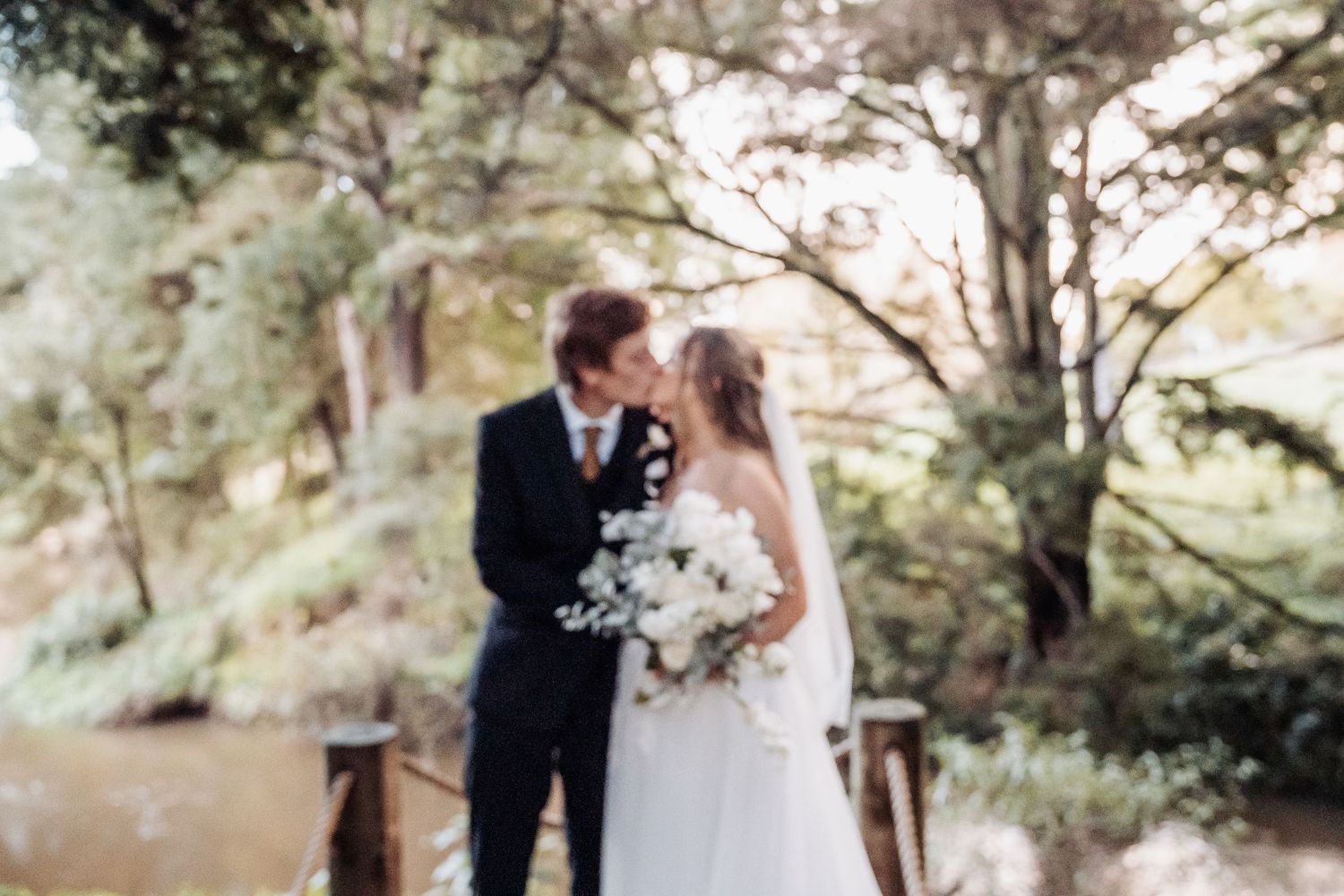 A romantic outdoor wedding portrait of a couple standing close together on a rustic wooden bridge.