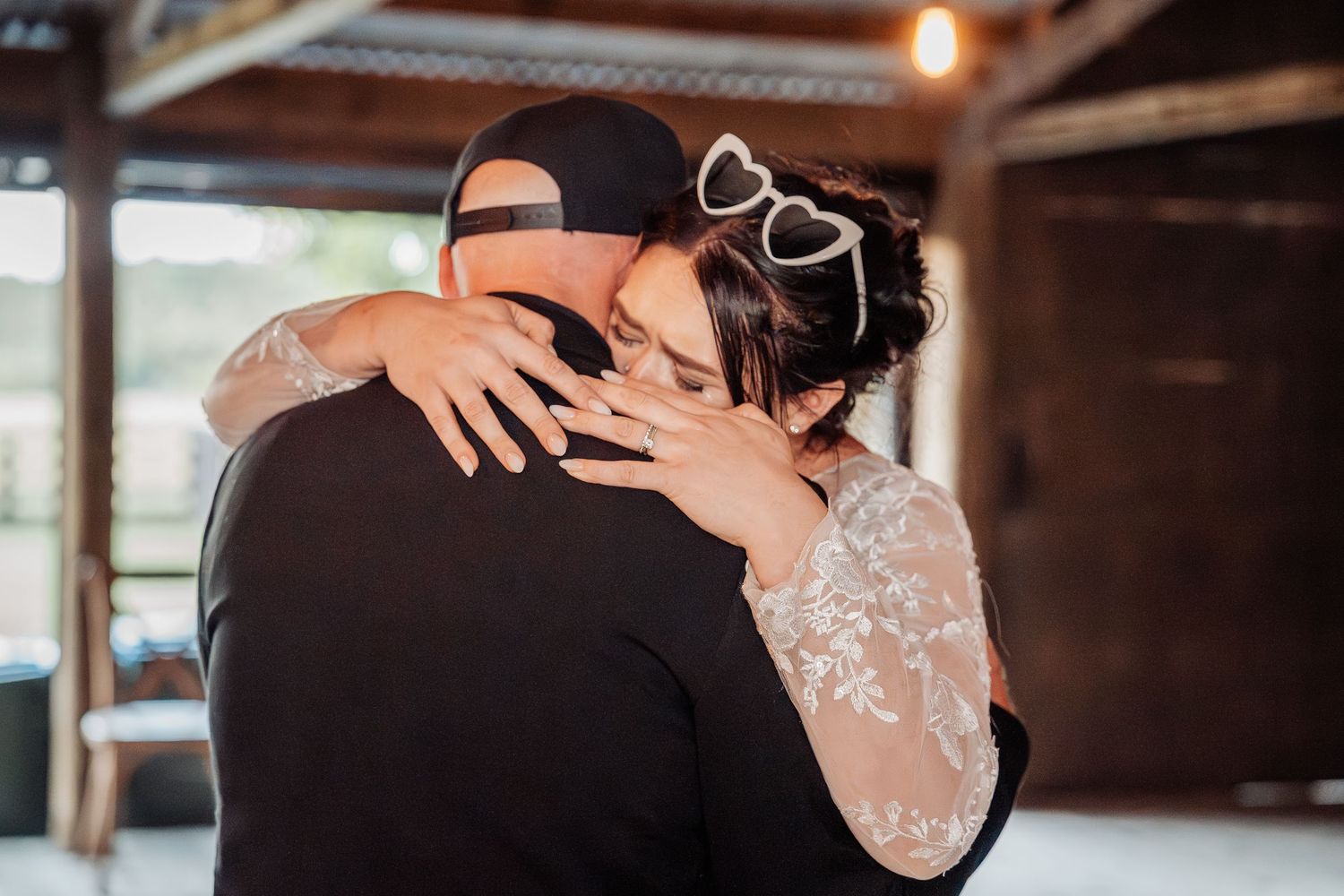 Intimate embrace during wedding dance captured in rustic indoor venue with warm lighting.