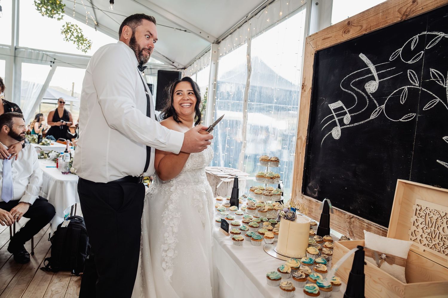 Bride and groom smile together near dessert table with cupcakes at their wedding reception.