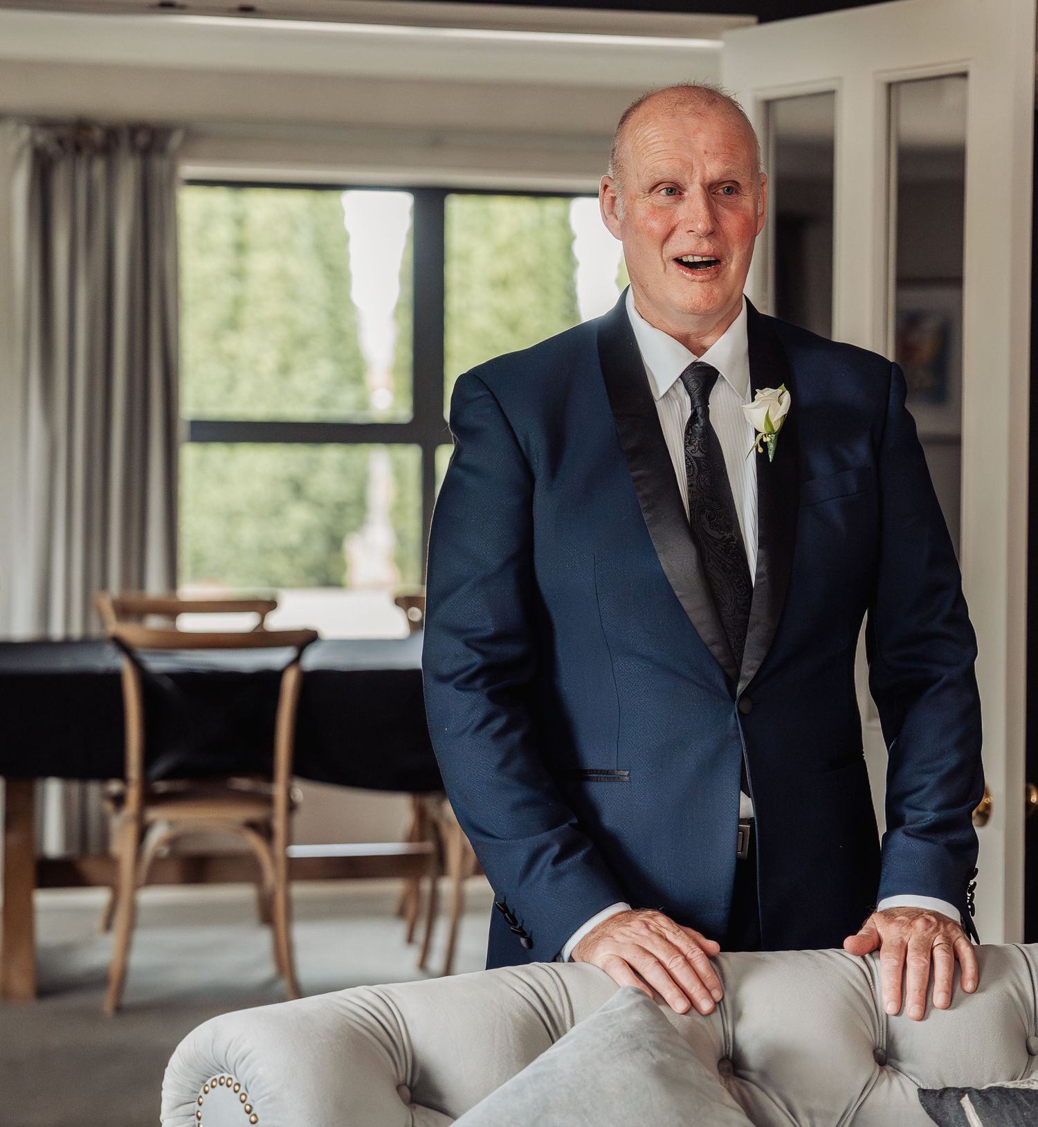 Man in navy blue suit with boutonniere smiling at wedding reception venue.