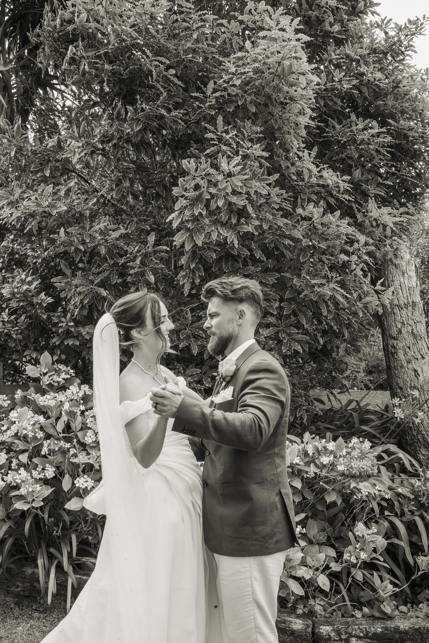 Black and white photo of bride and groom dancing romantically in a lush garden.