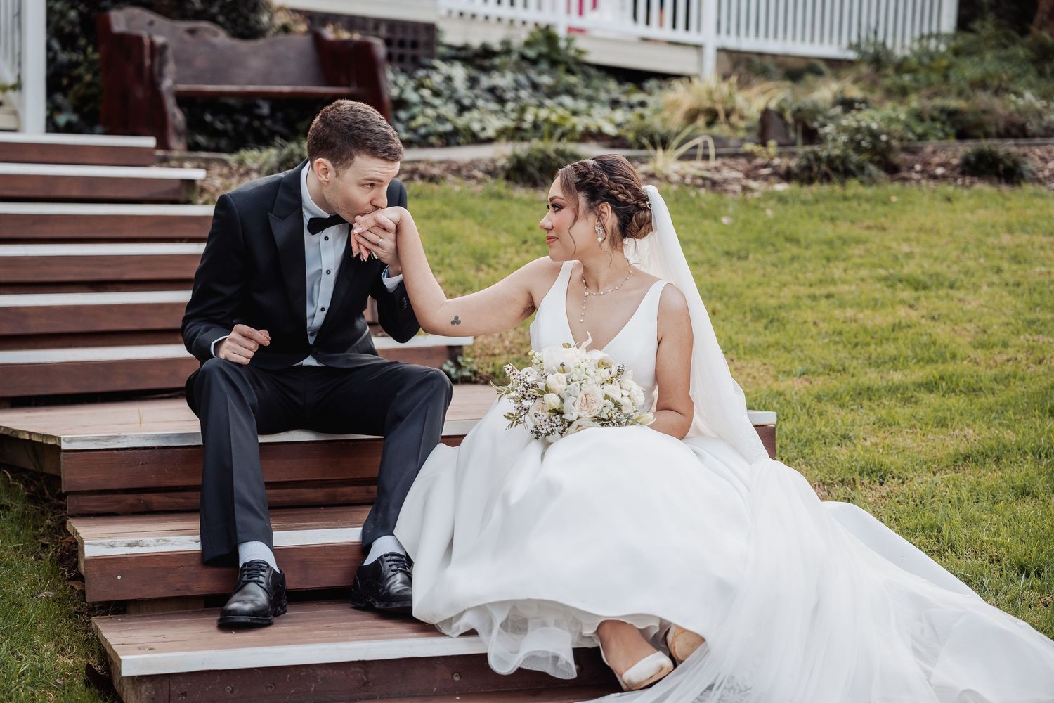 Newlyweds sitting together on wooden steps in garden setting.