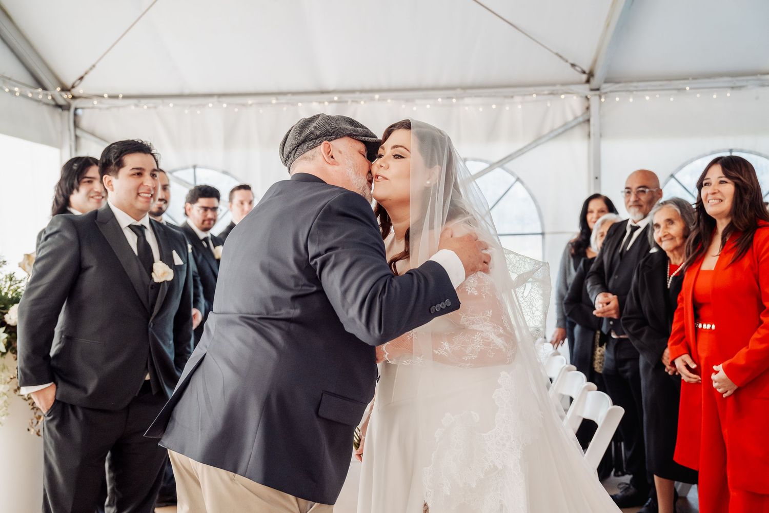 Emotional wedding ceremony moment under a white tent with guests watching and celebrating as a couple embraces.
