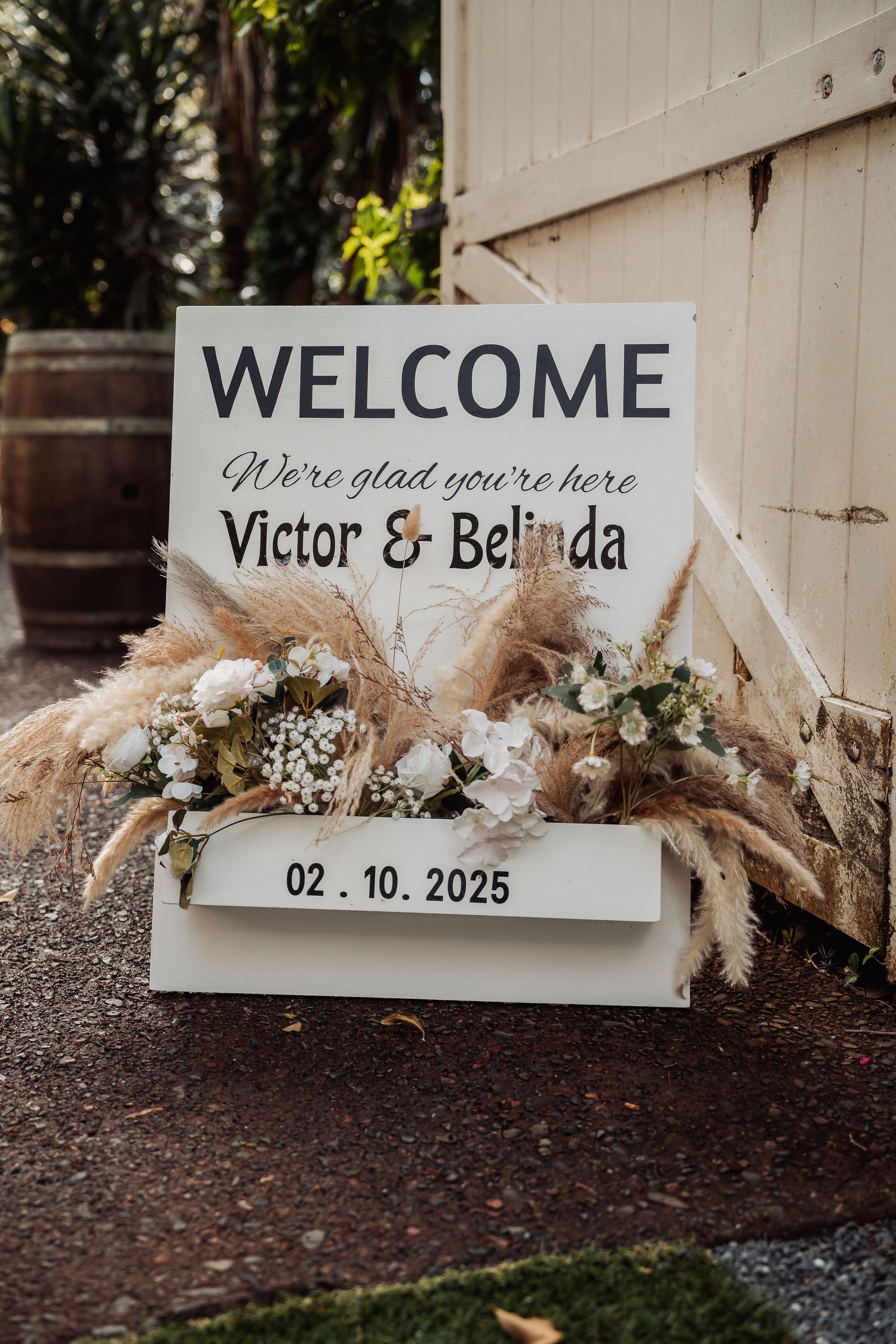 Rustic wedding welcome sign decorated with dried pampas grass and white floral arrangements.