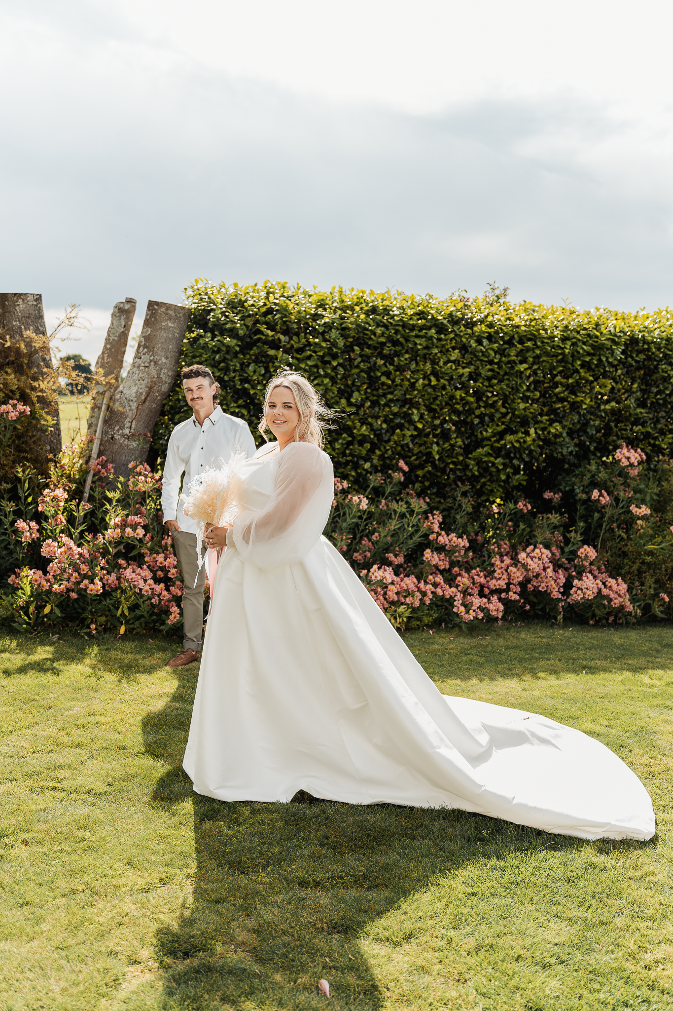 Wedding couple posing in garden with flowing white dress and floral backdrop.