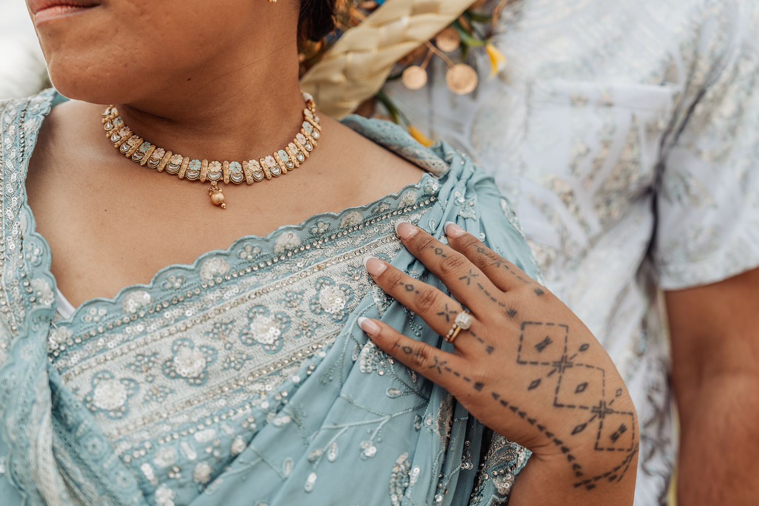 Detailed view of traditional henna design on hand against light blue embroidered sari.