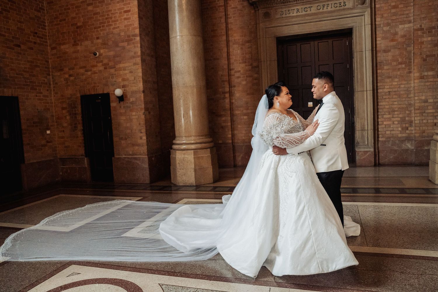 Wedding couple embracing in an elegant brick-lined hallway with ornate architectural details.