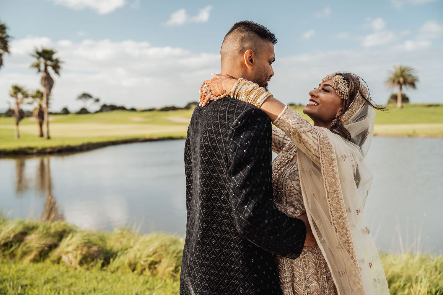 Romantic photoshoot by a lake with palm trees and natural scenery in the background.