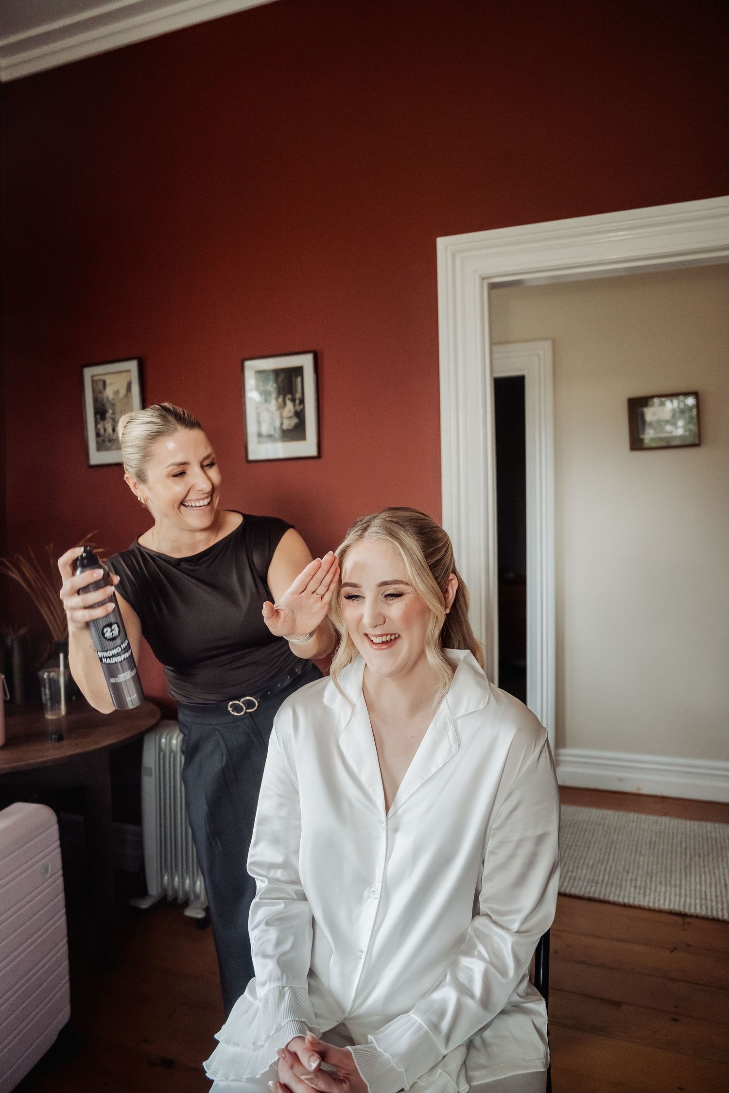 A candid moment shows laughter and joy during wedding preparations in a room with burgundy walls.