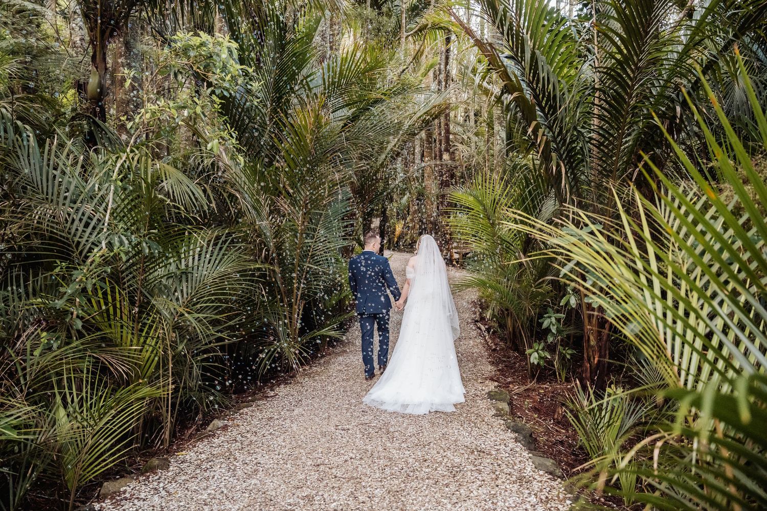 A winding garden path lined with lush palm fronds and tropical foliage creates a natural wedding aisle.