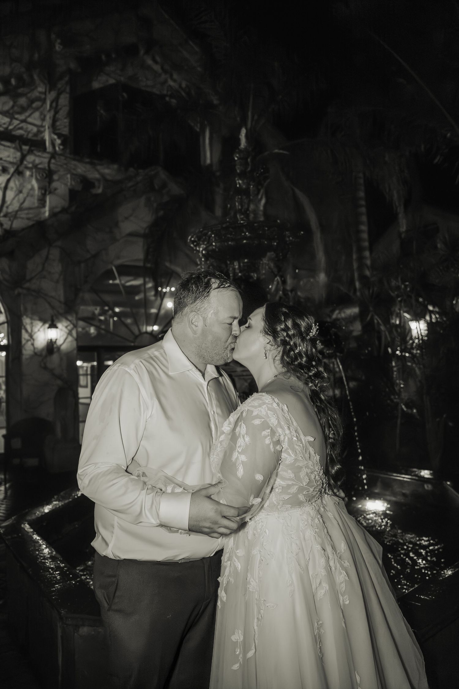Romantic nighttime portrait of newlyweds sharing an intimate moment under garden lights.