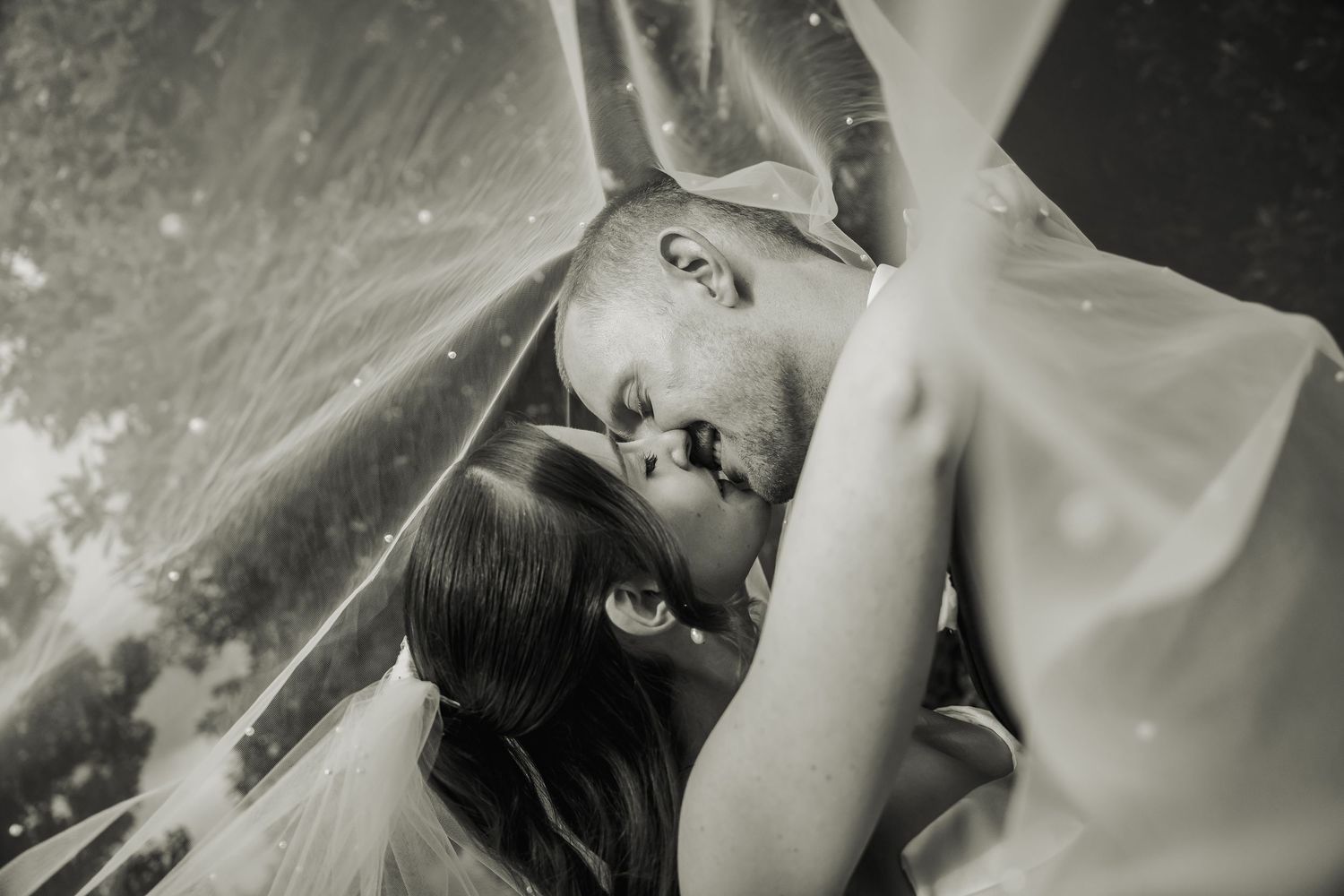 Romantic black and white under-veil kiss photo of bride and groom on wedding day.