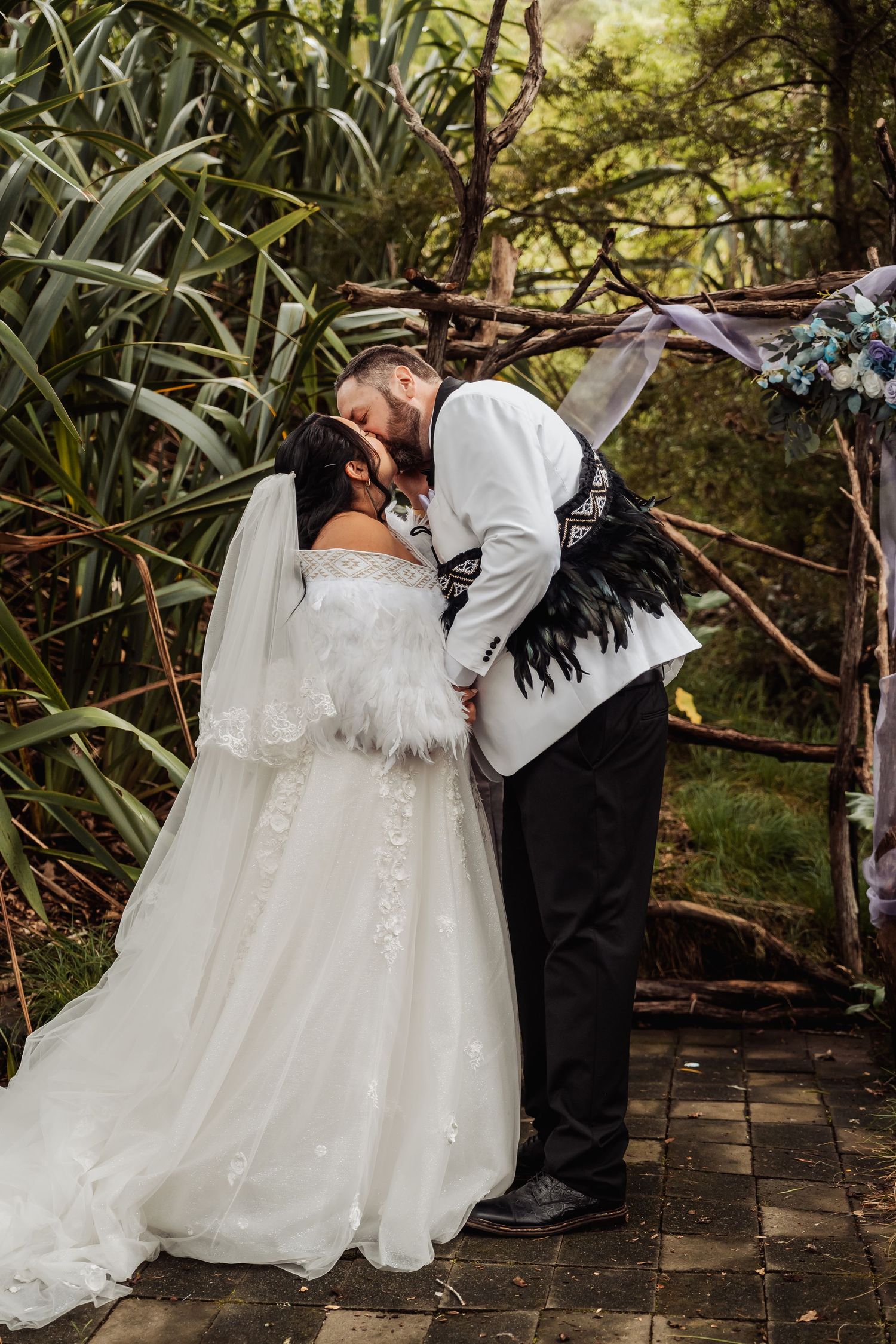 Bride and groom share first kiss at rustic outdoor woodland wedding ceremony.