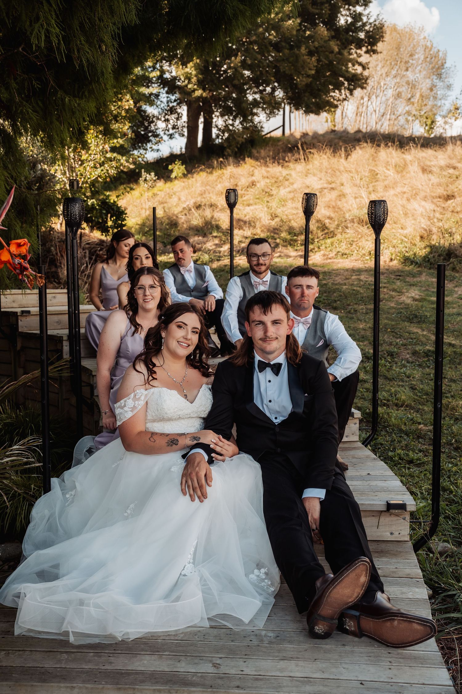Wedding party poses together on a wooden deck at golden hour with bride and groom seated in front.