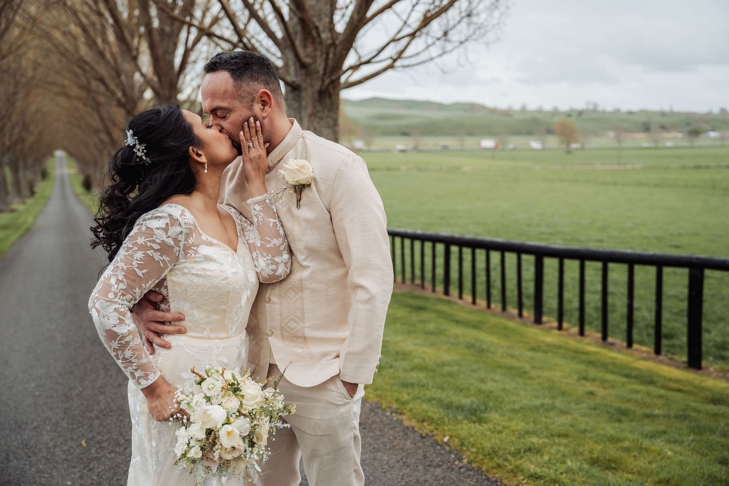 Intimate wedding portrait on a scenic country road lined with bare trees and green pastures.