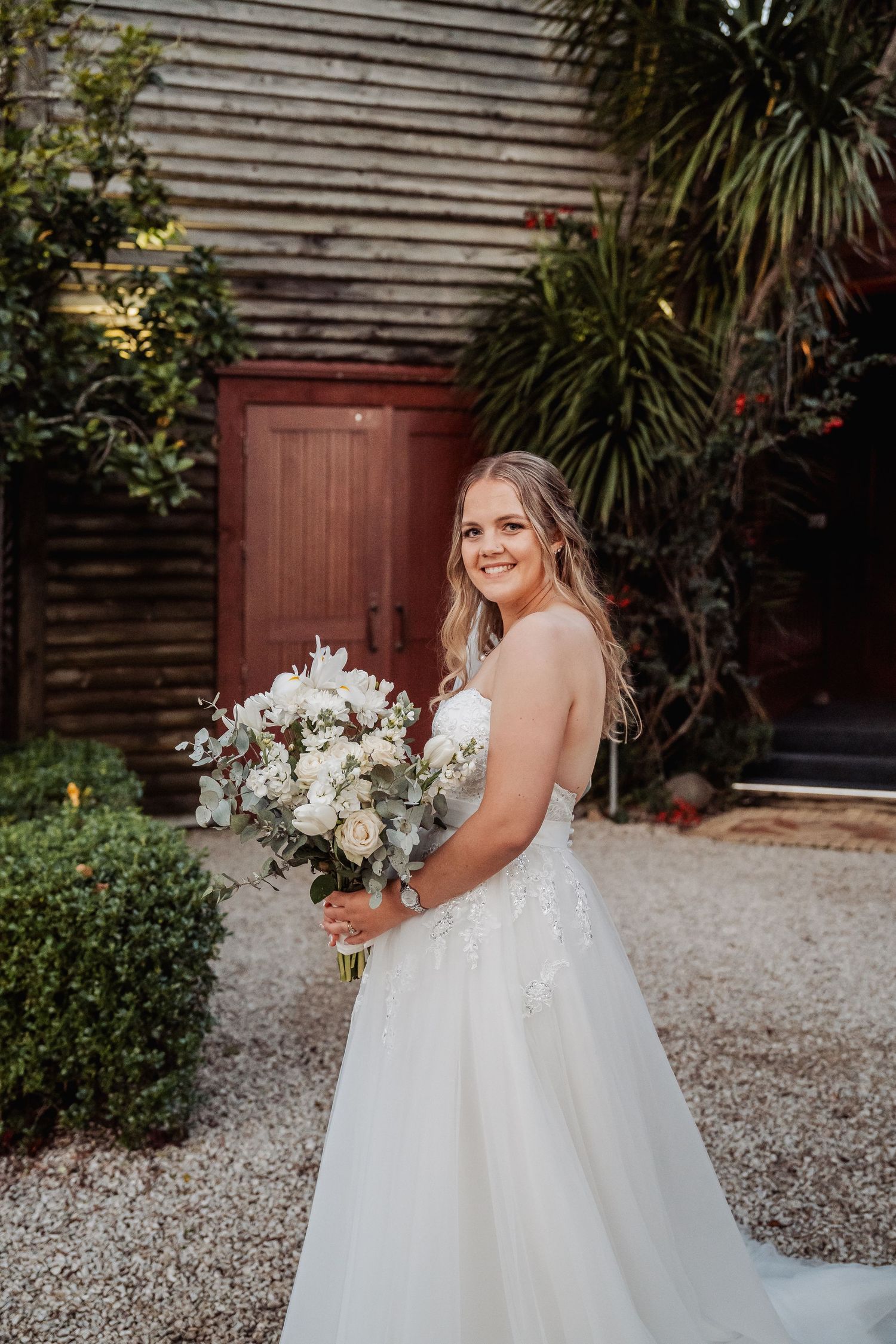 Beautiful wedding bouquet with white flowers against rustic wooden wall and gravel path.
