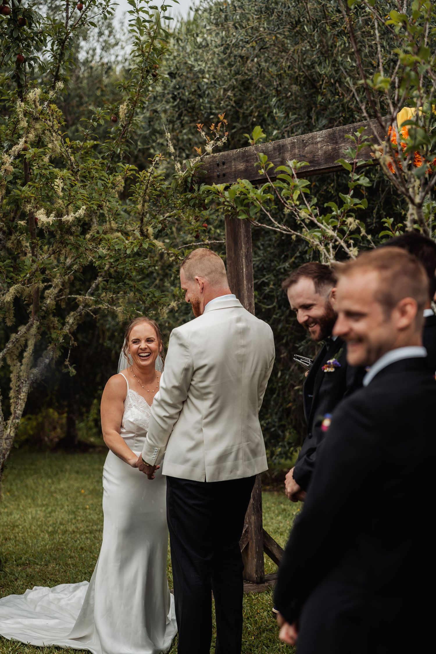 Joyful bride laughing with groom during outdoor wedding ceremony under rustic wooden arch.