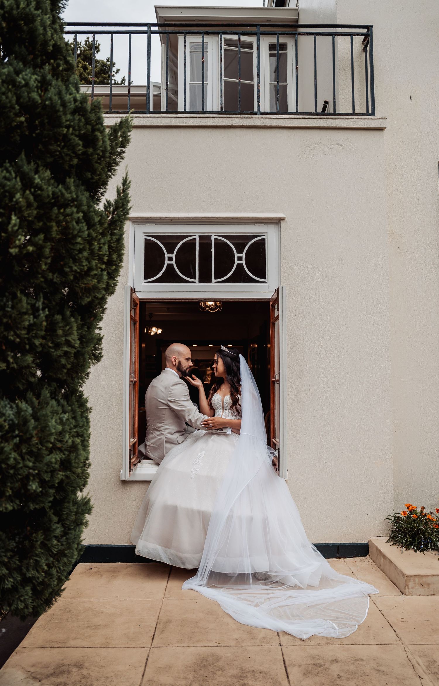 Bride and groom share romantic moment in doorway, bride wearing flowing white gown with long veil at wedding venue.