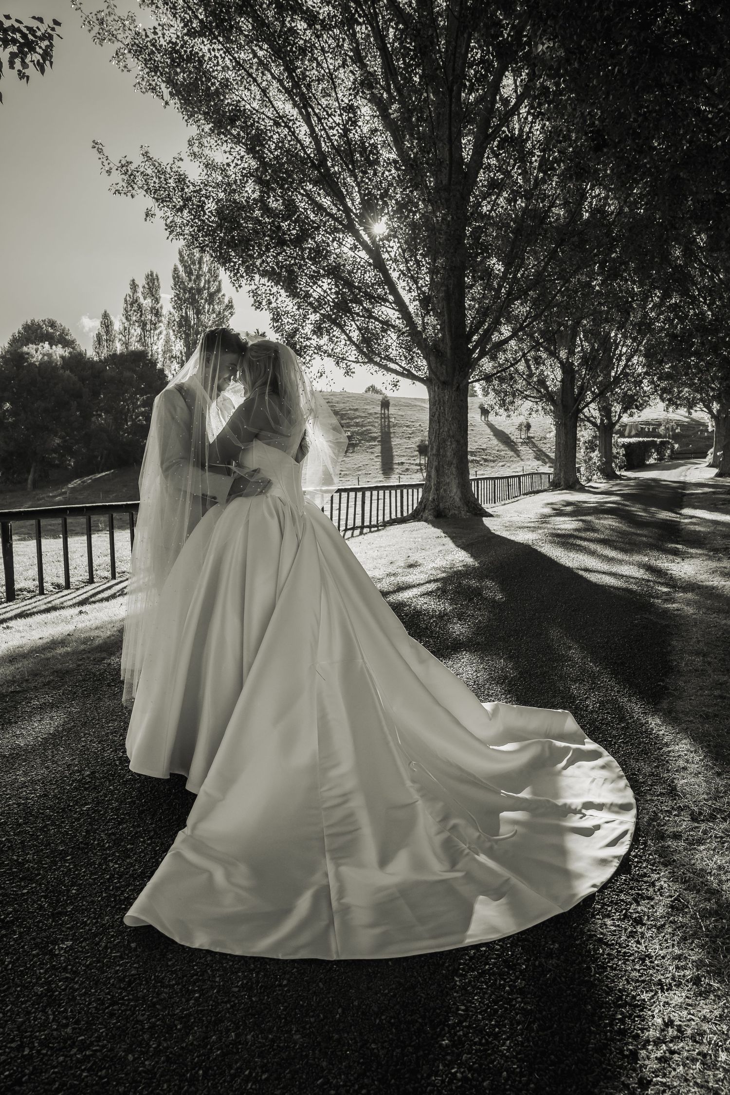 Black and white photo of bride and groom embracing under tall trees on their wedding day.