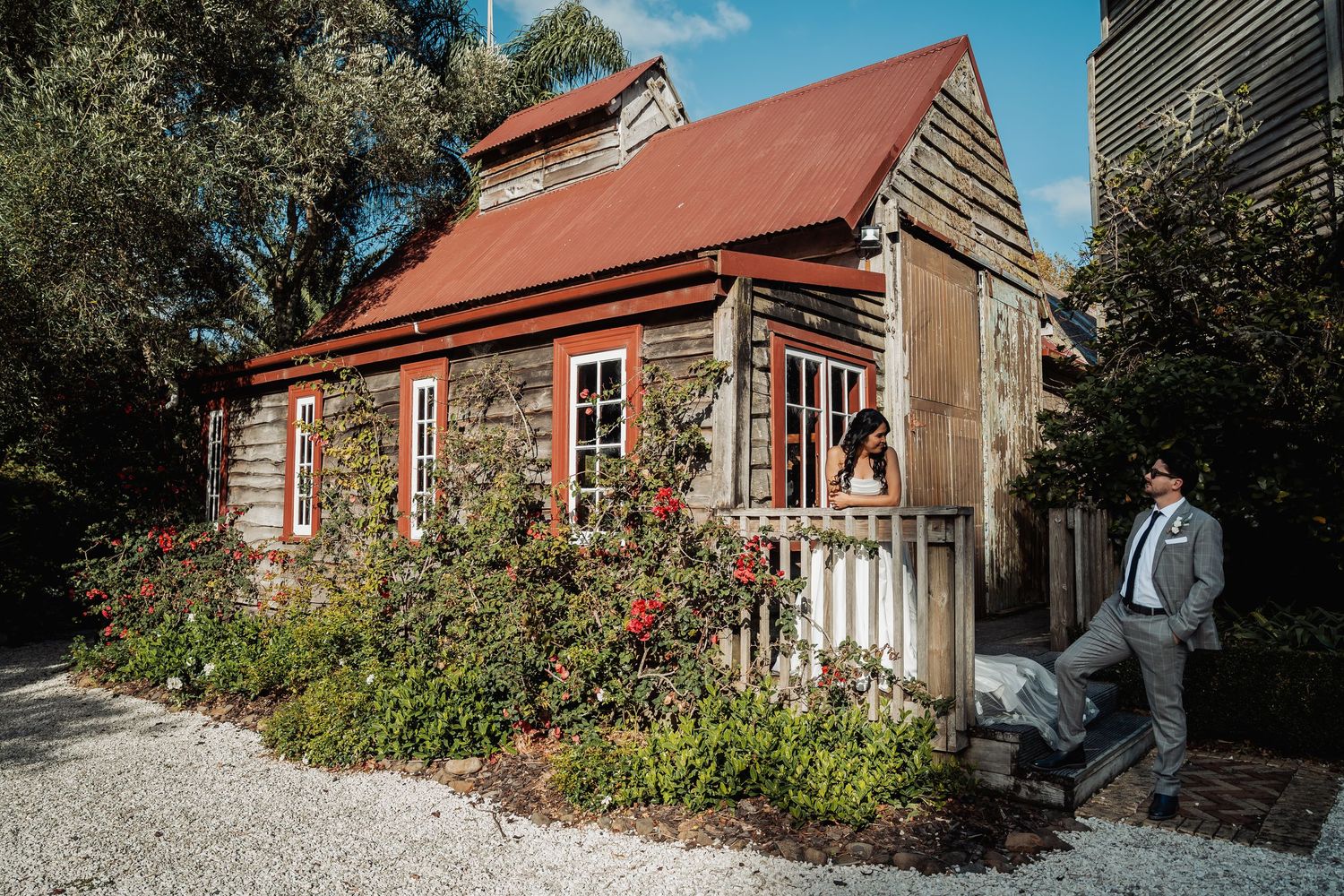 Rustic wooden cottage with red roof surrounded by blooming roses and lush greenery at a wedding venue.