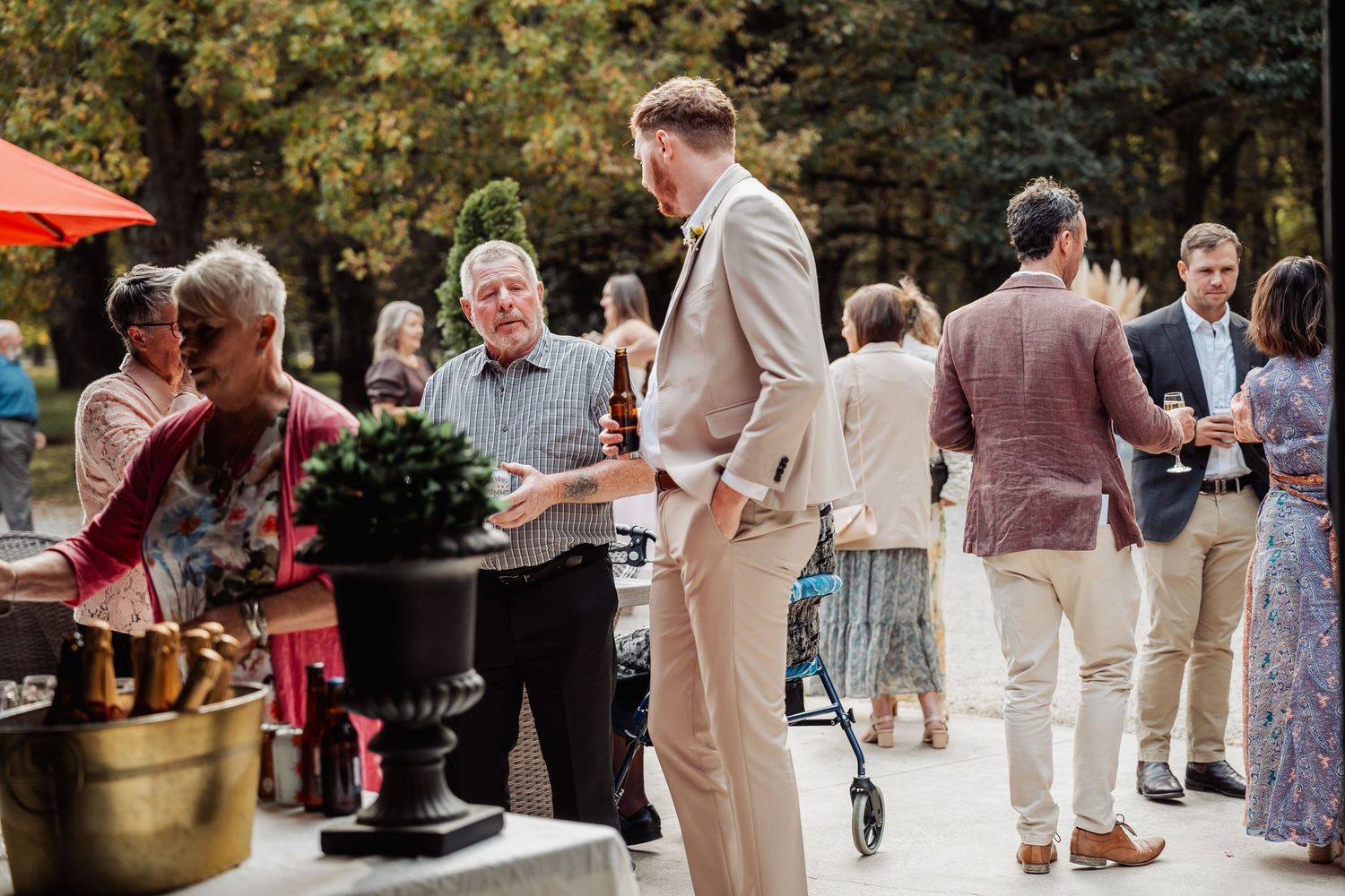 Wedding guests mingling outdoors on a patio surrounded by trees at a garden reception.
