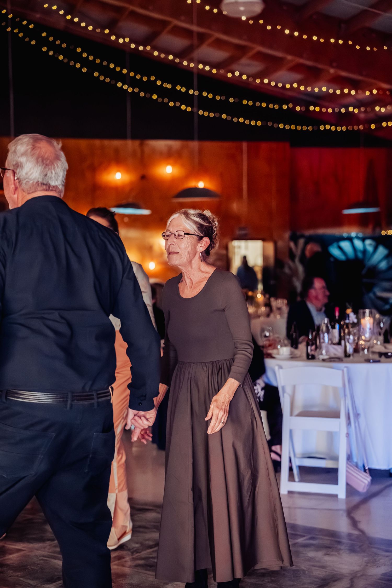 Woman in brown dress dancing with partner at warmly lit wedding reception venue.