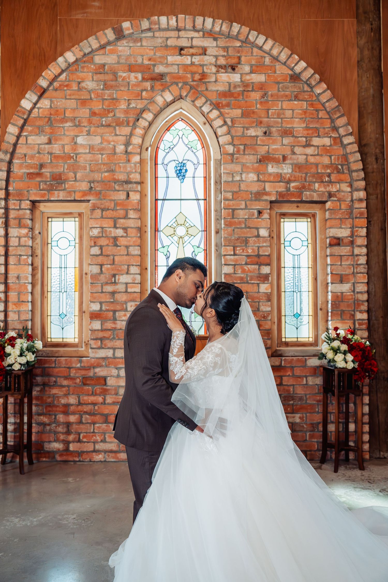 Bride and groom sharing a romantic moment in a chapel with brick walls and stained glass windows.