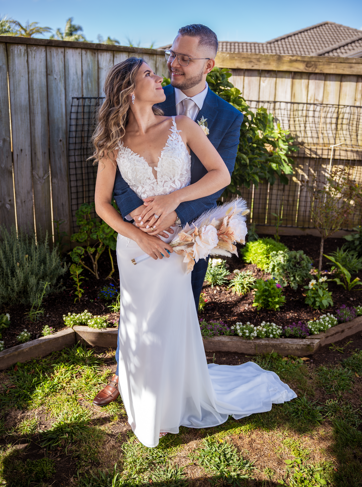 A tender embrace between newlyweds in a sunny garden with decorative landscaping.