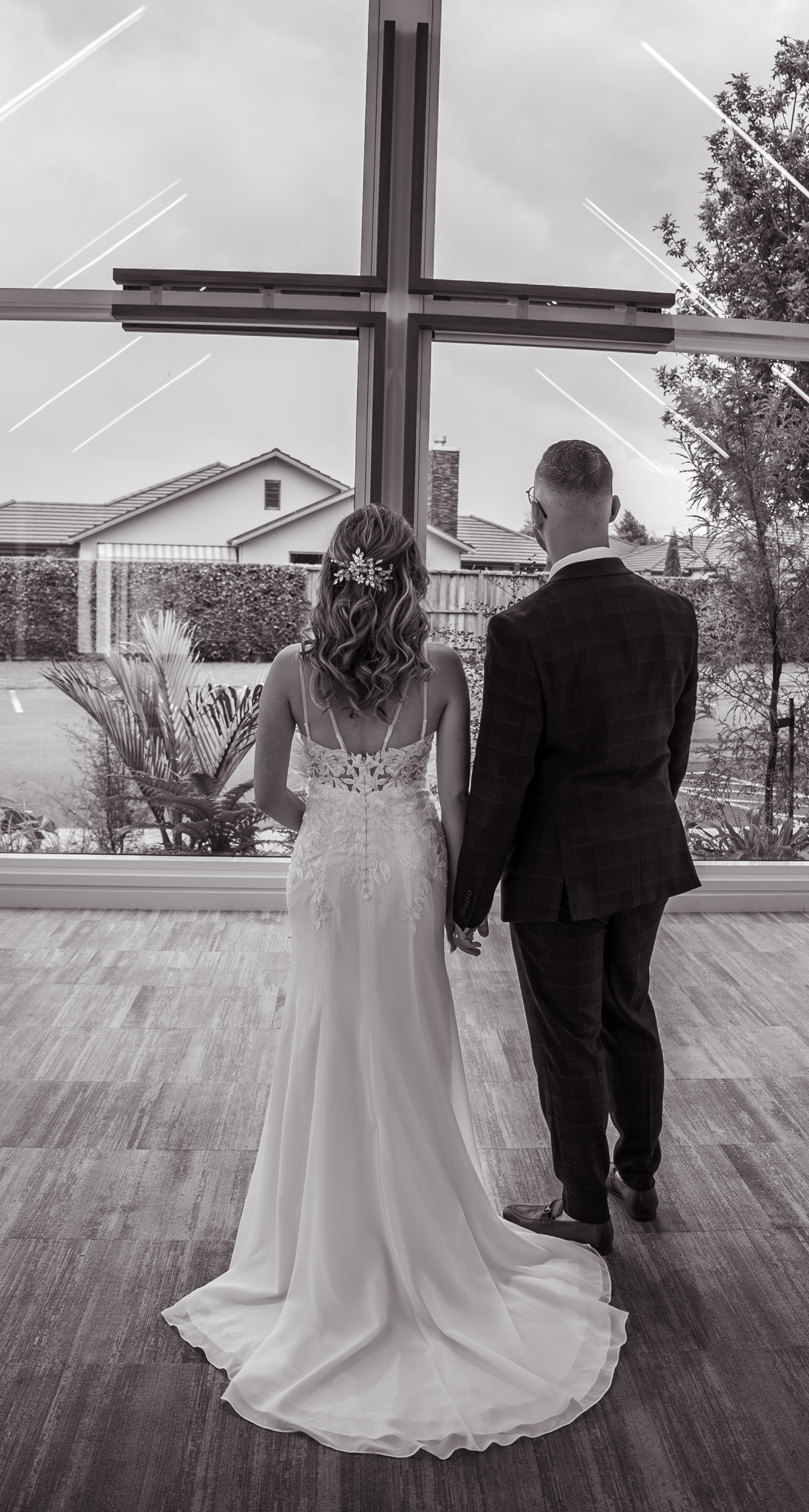 A wedding couple stands before a large cross in a church sanctuary, captured in black and white.