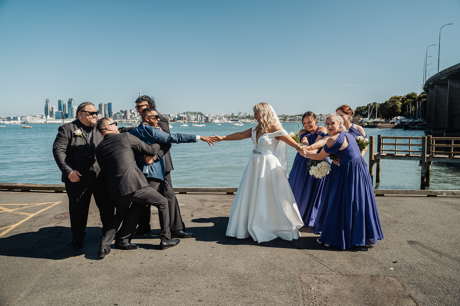 Wedding party poses playfully on a pier with city skyline in the background.