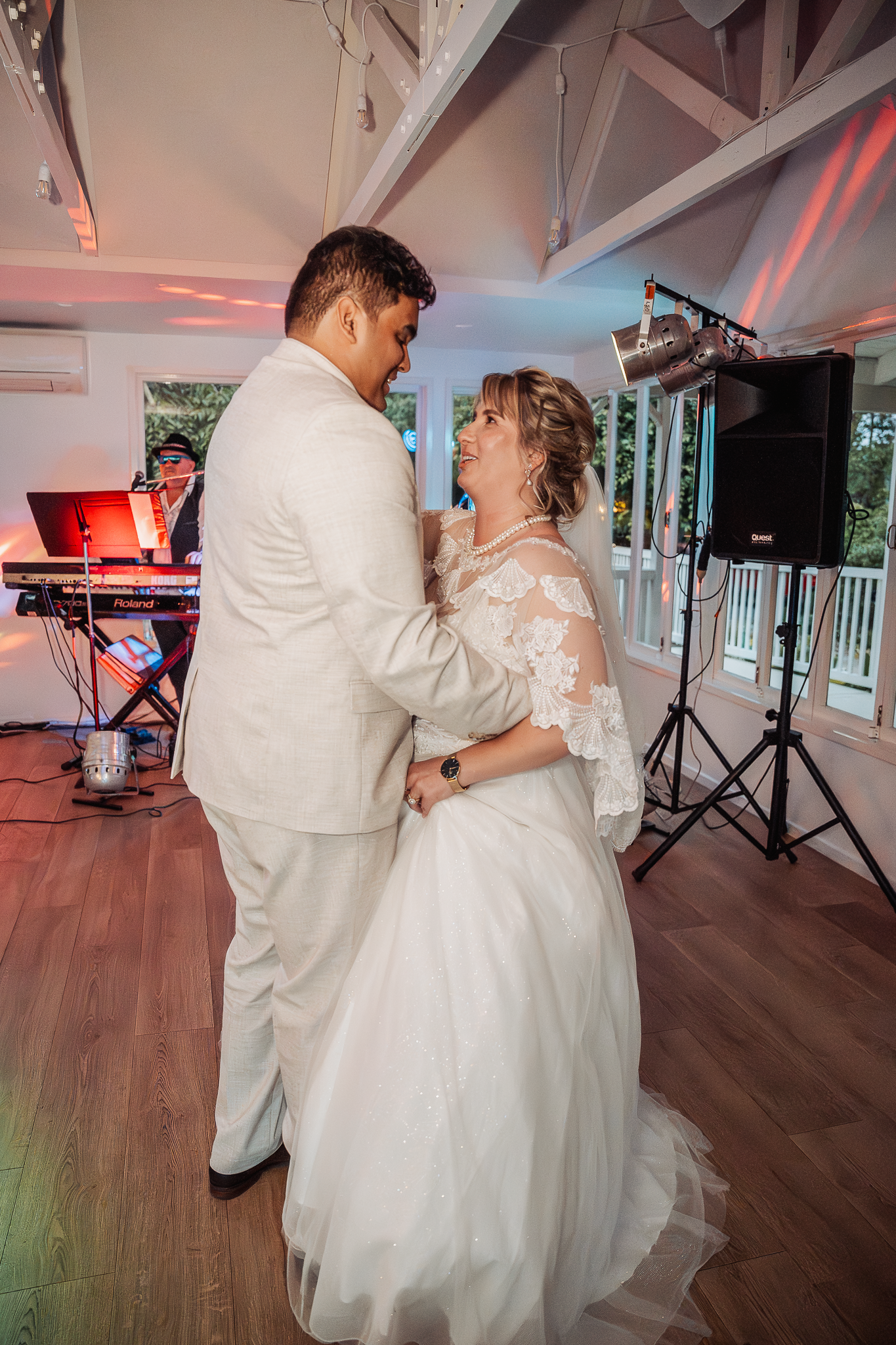 A couple shares their first dance at their wedding reception under red mood lighting.