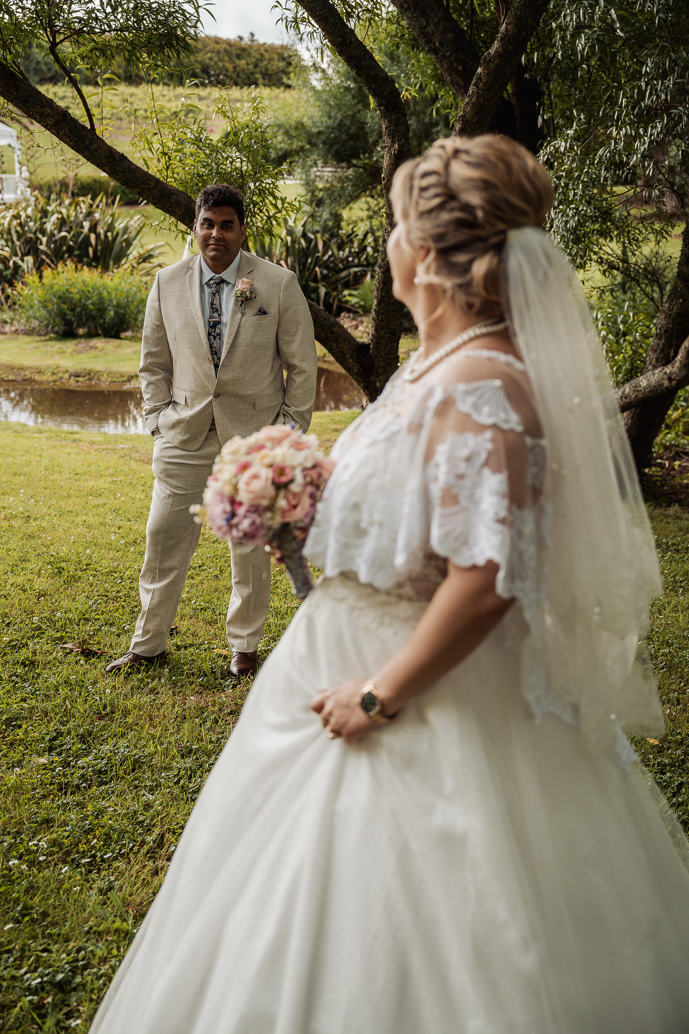 A couple taking wedding photos in a garden setting with the bride wearing a traditional white gown with lace details.