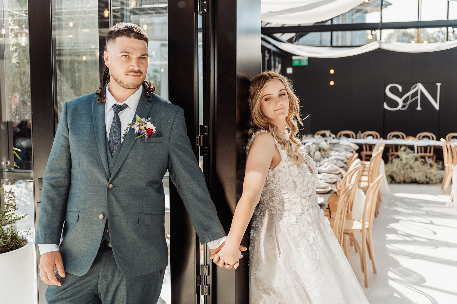 Wedding couple in formal attire stand together outside venue entrance.