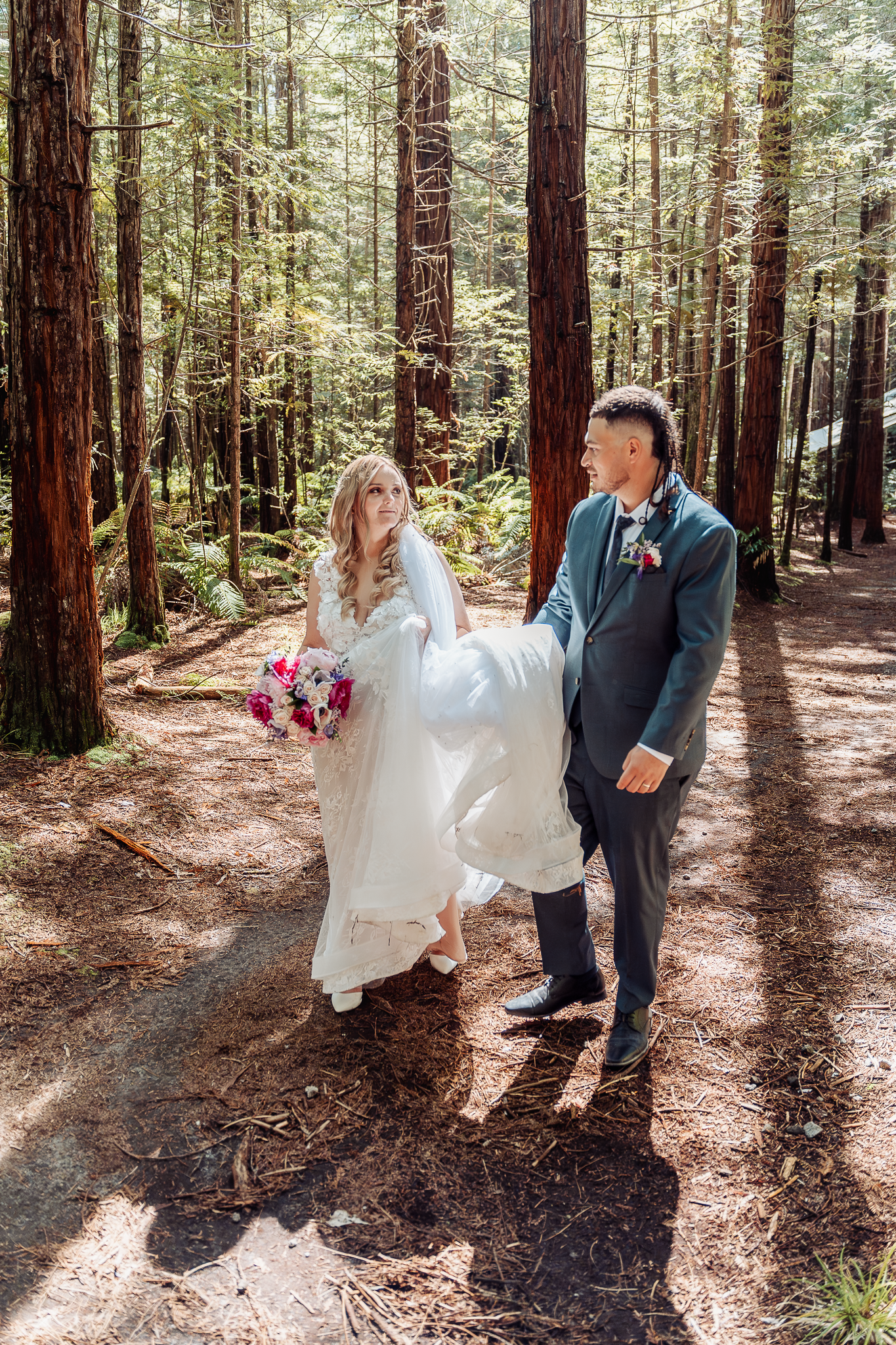 Wedding couple posing on forest trail surrounded by towering redwood trees.