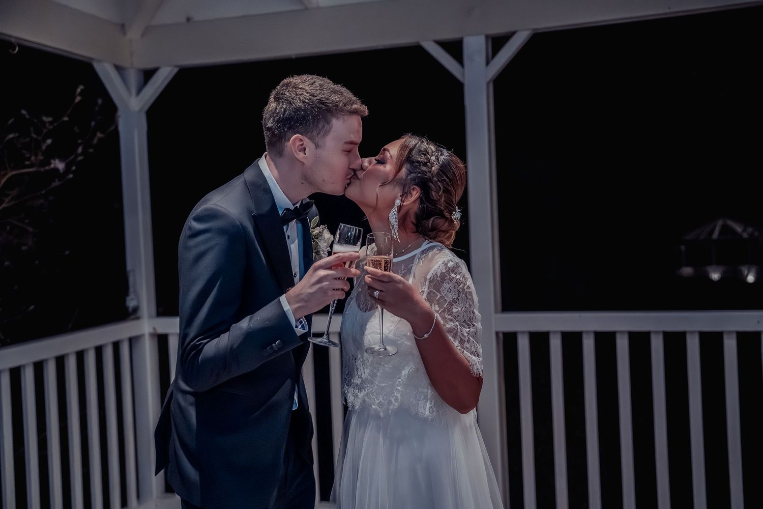 Evening wedding ceremony under white gazebo with romantic lighting.