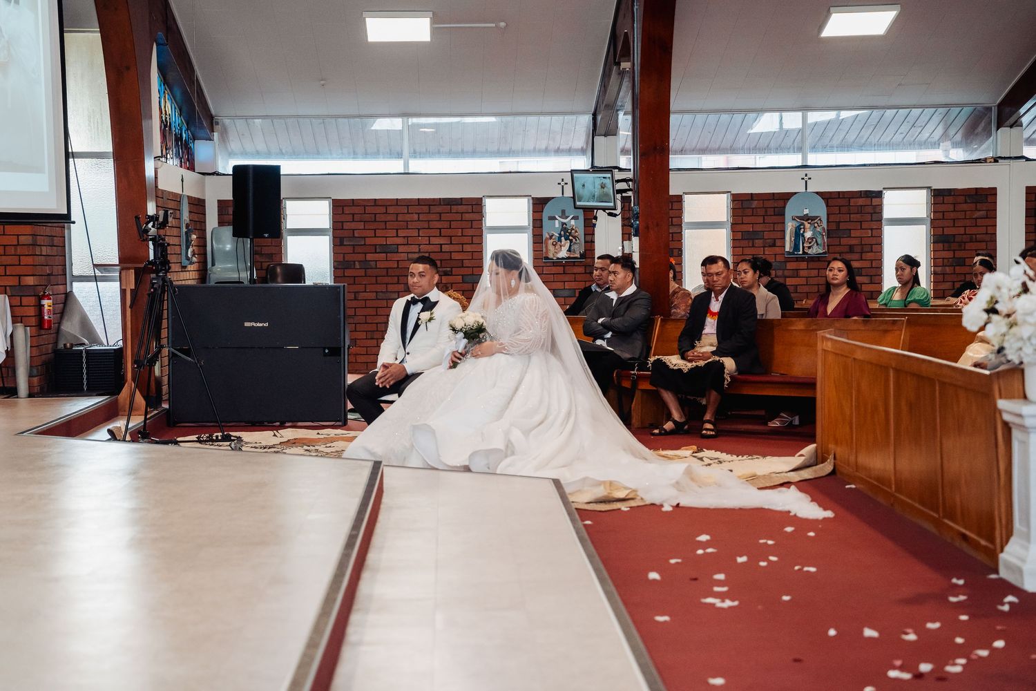 Wedding ceremony held in a brick-walled room with red carpet and scattered flower petals.