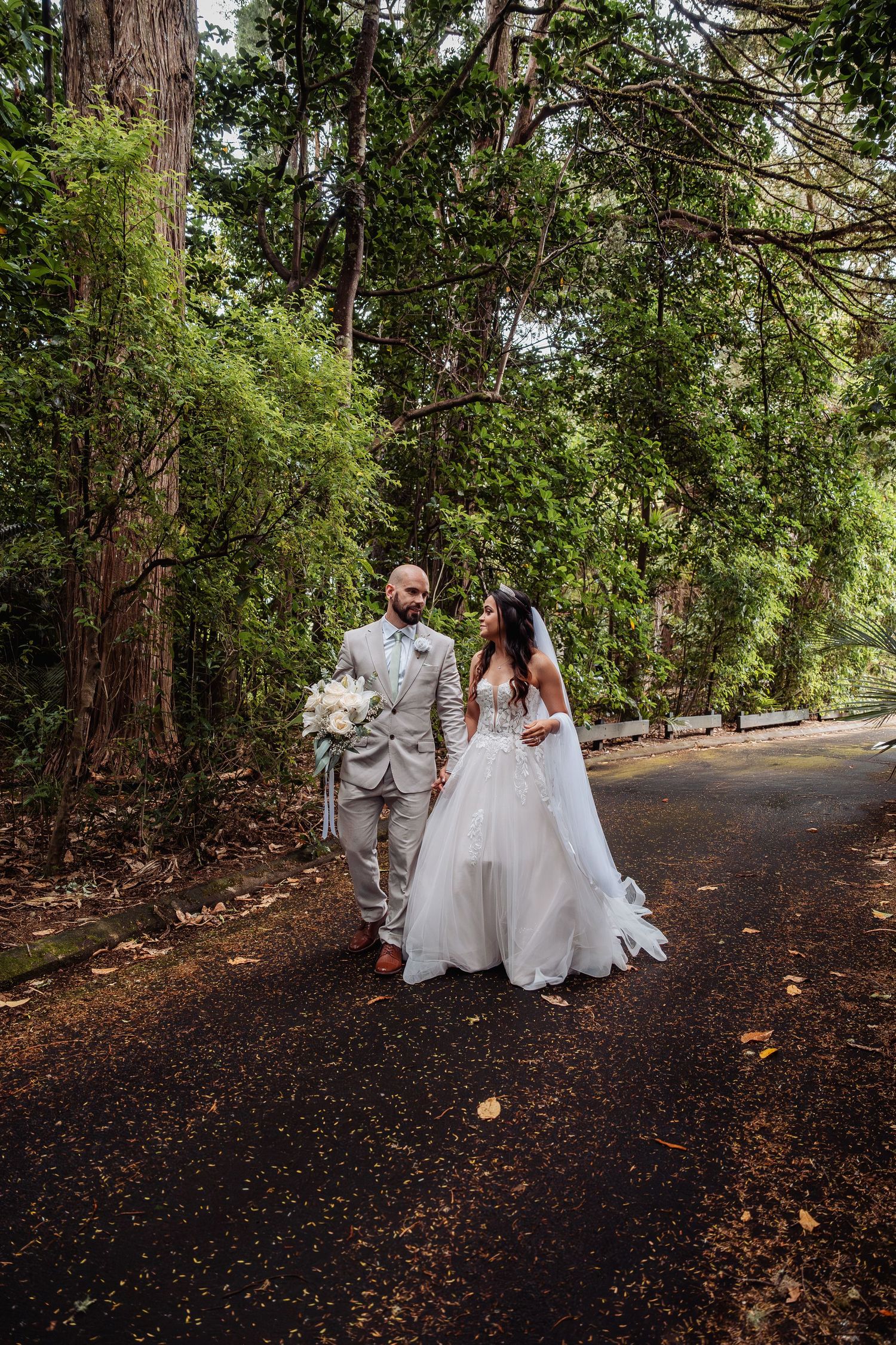 Bride and groom walk hand in hand along tree-lined path in stunning forest wedding portrait.