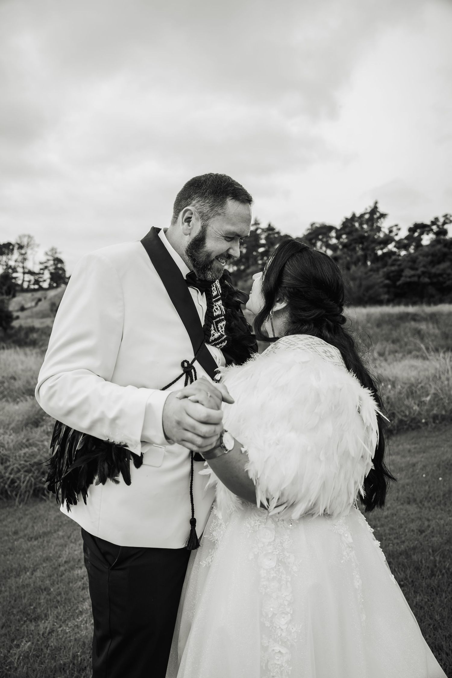 Black and white photo of bride and groom sharing intimate moment holding hands on grassy field.