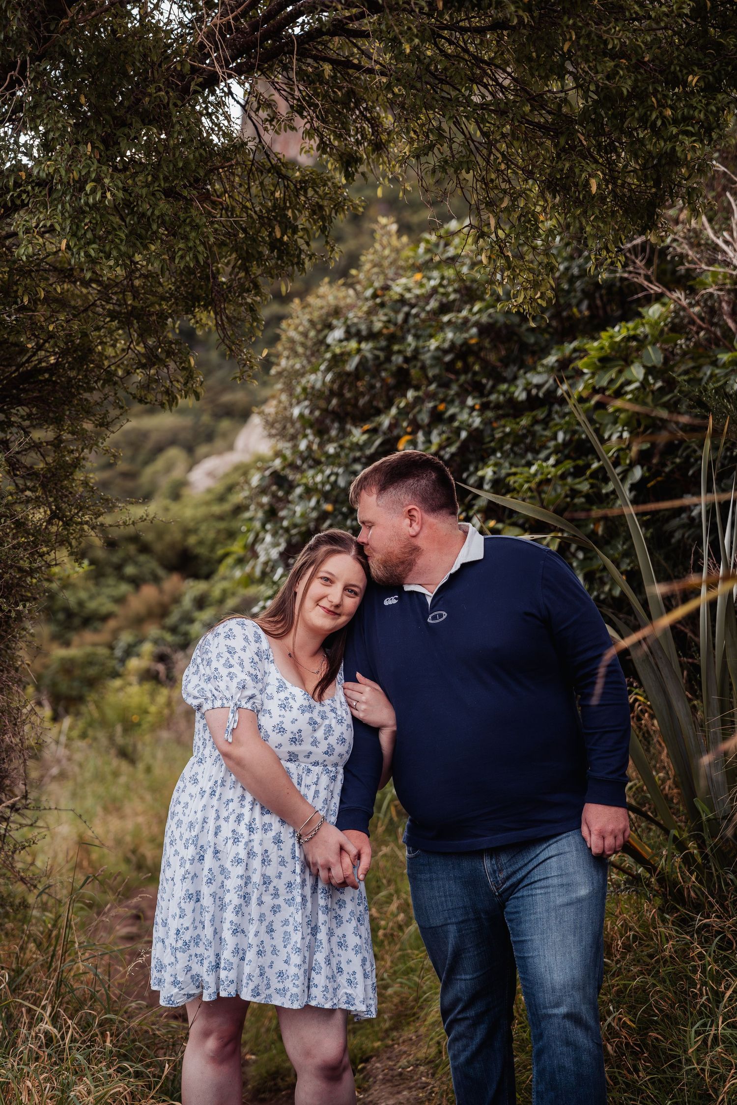 Couple walking hand in hand along a leafy bush trail, sharing a romantic glance at each other.