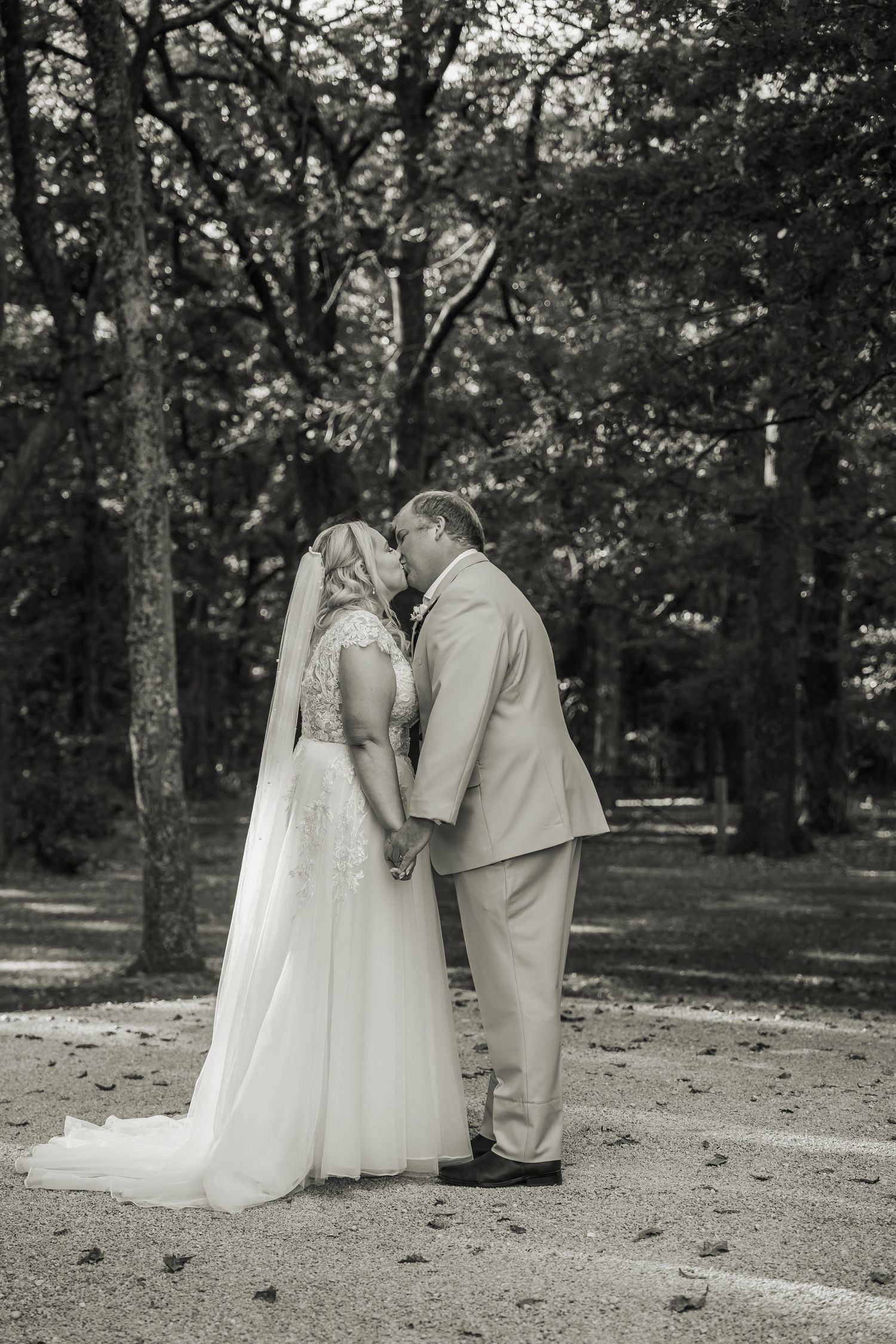 Bride and groom sharing a romantic kiss in black and white photo among lush forest trees.