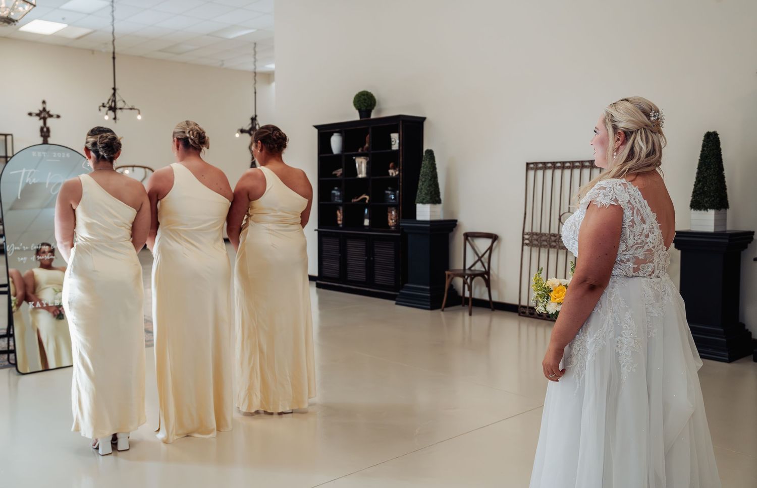 Bride reveals wedding dress to bridesmaids in cream gowns during emotional first look moment.