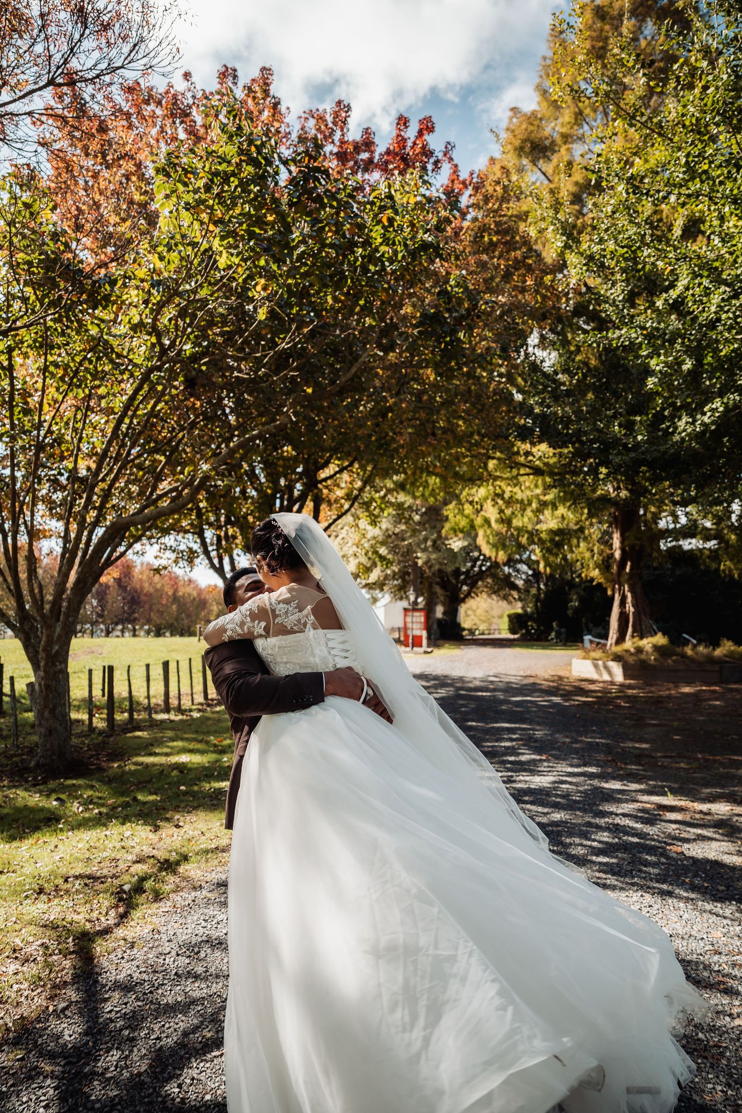 Bride and groom embracing on a tree-lined path in autumn setting.