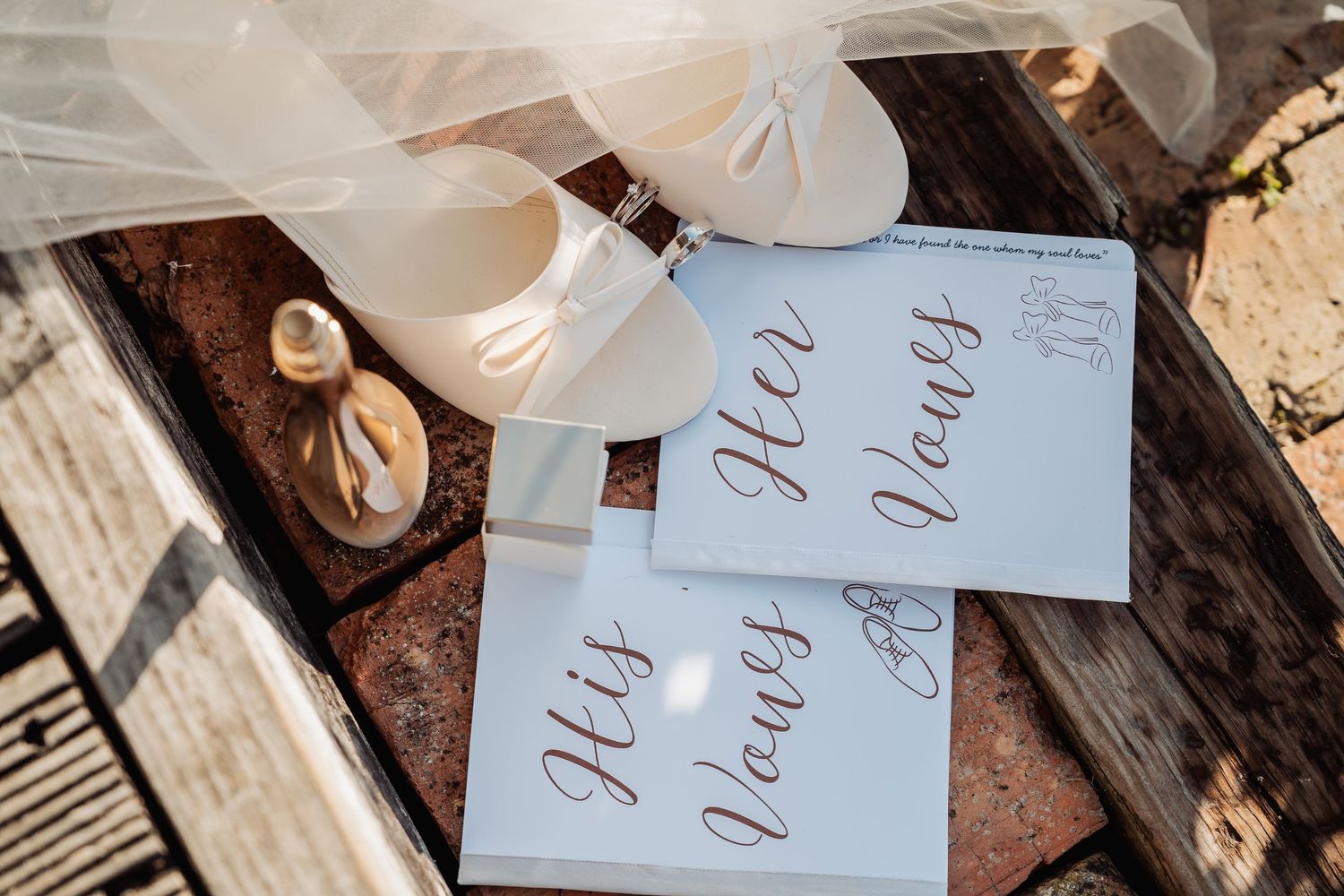 His and Her Vows cards displayed beside white bridal heels and perfume on rustic wooden steps.