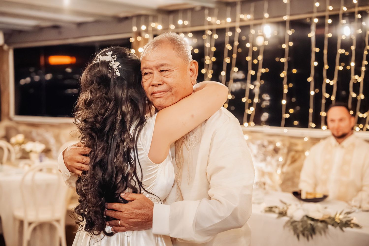Emotional dance moment captured at wedding reception with twinkling lights in background.