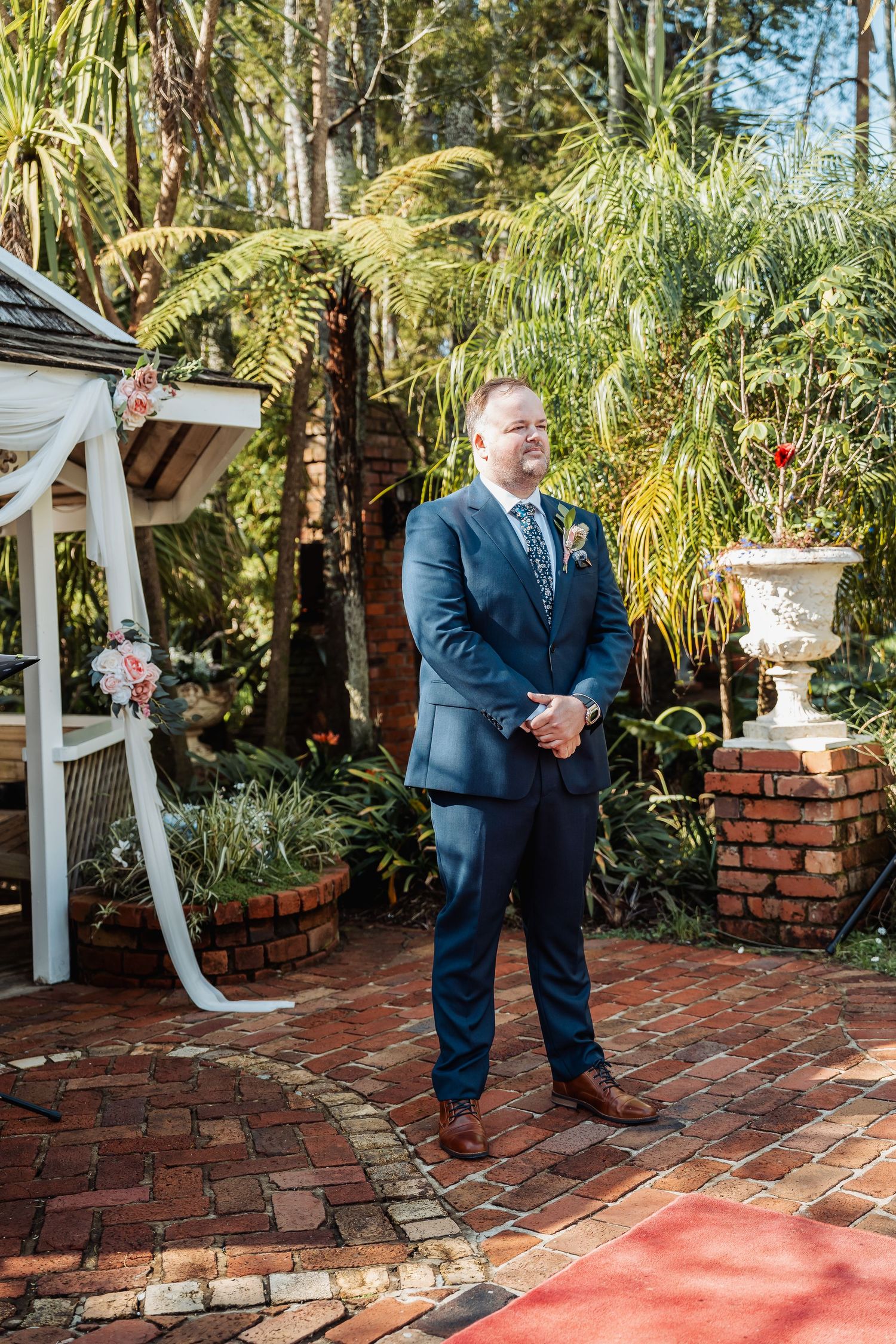 Wedding ceremony setup with brick patio, red carpet aisle, and tropical palm garden backdrop.